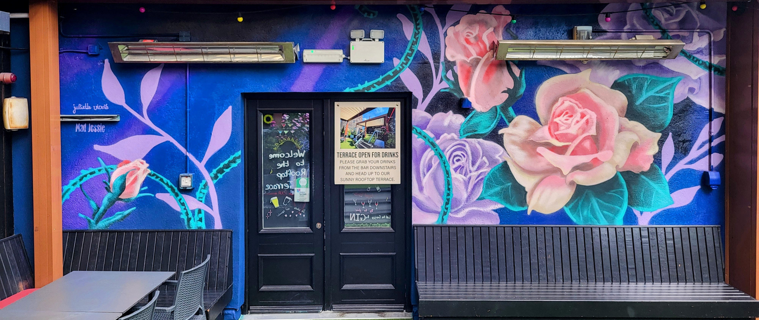 A large mural with blue background with pink and purple roses in the foreground 