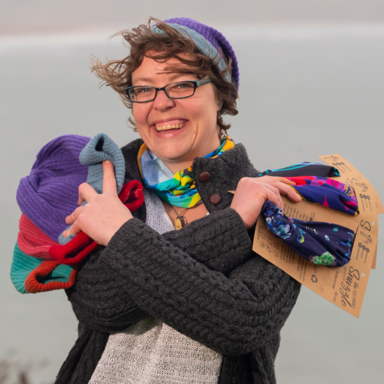 Mad Jessie holding products from Mad jessie shop multicolored knitted hats and snuzzles